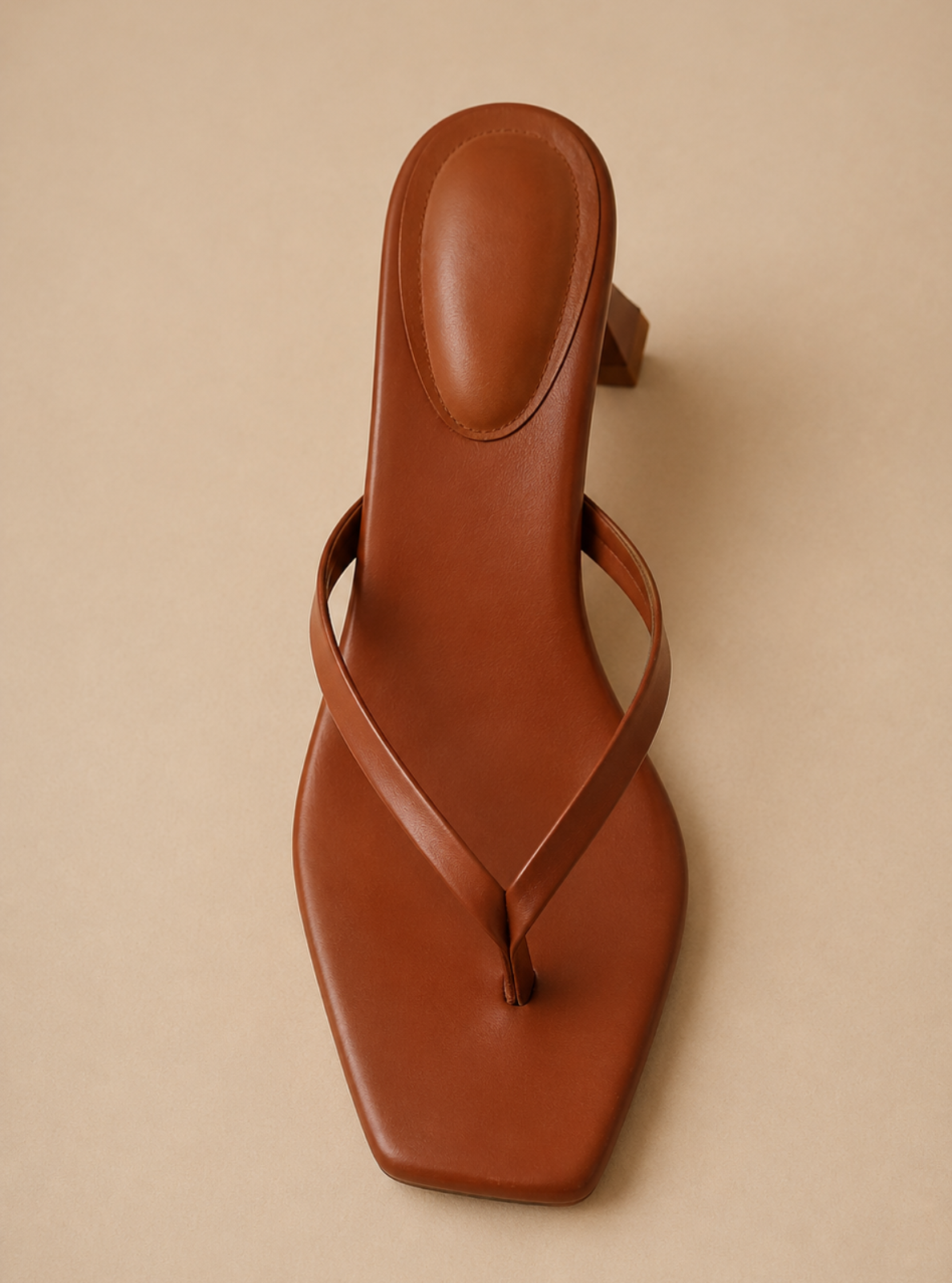 A single brown leather thong sandal with a square toe and a low block heel, photographed from a top-down angle on a solid beige background.