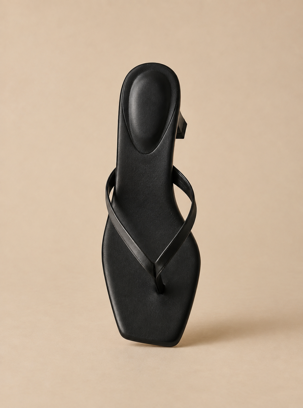 A single black leather thong sandal with a square toe and a low block heel, shown from a top-down angle on a solid beige background.