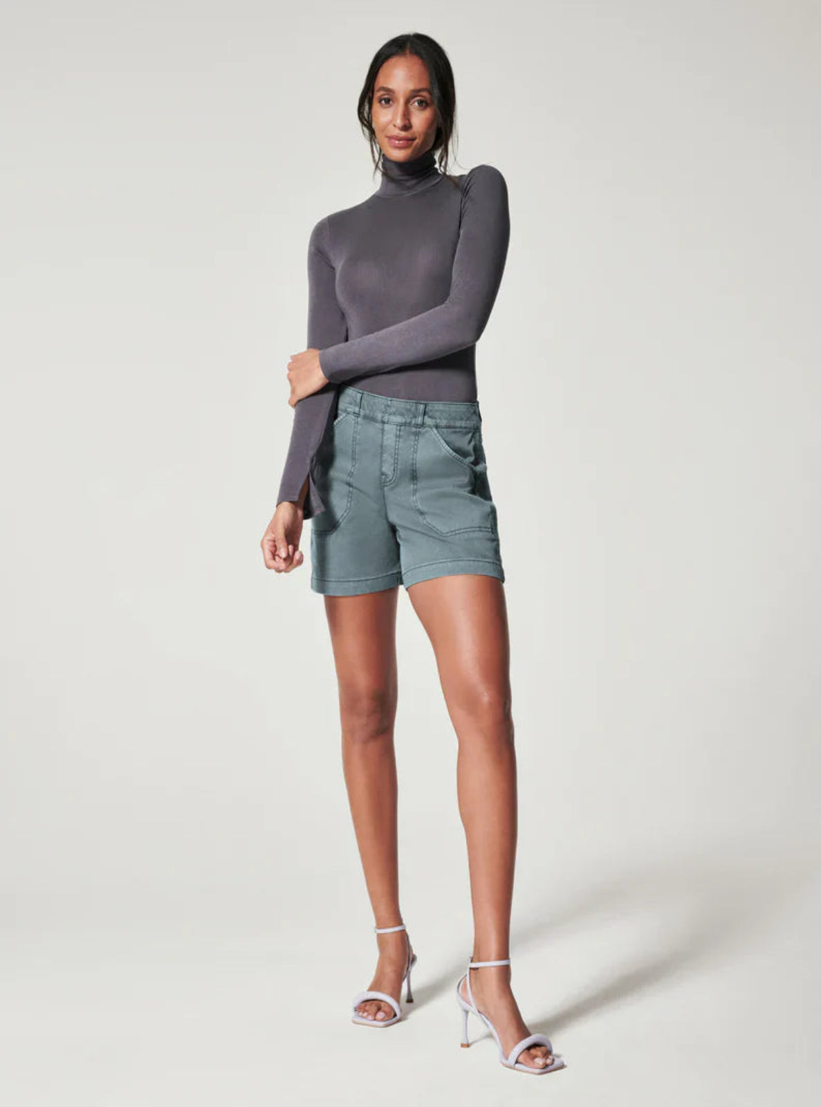 Woman wearing a gray turtleneck and light blue shorts on a white background