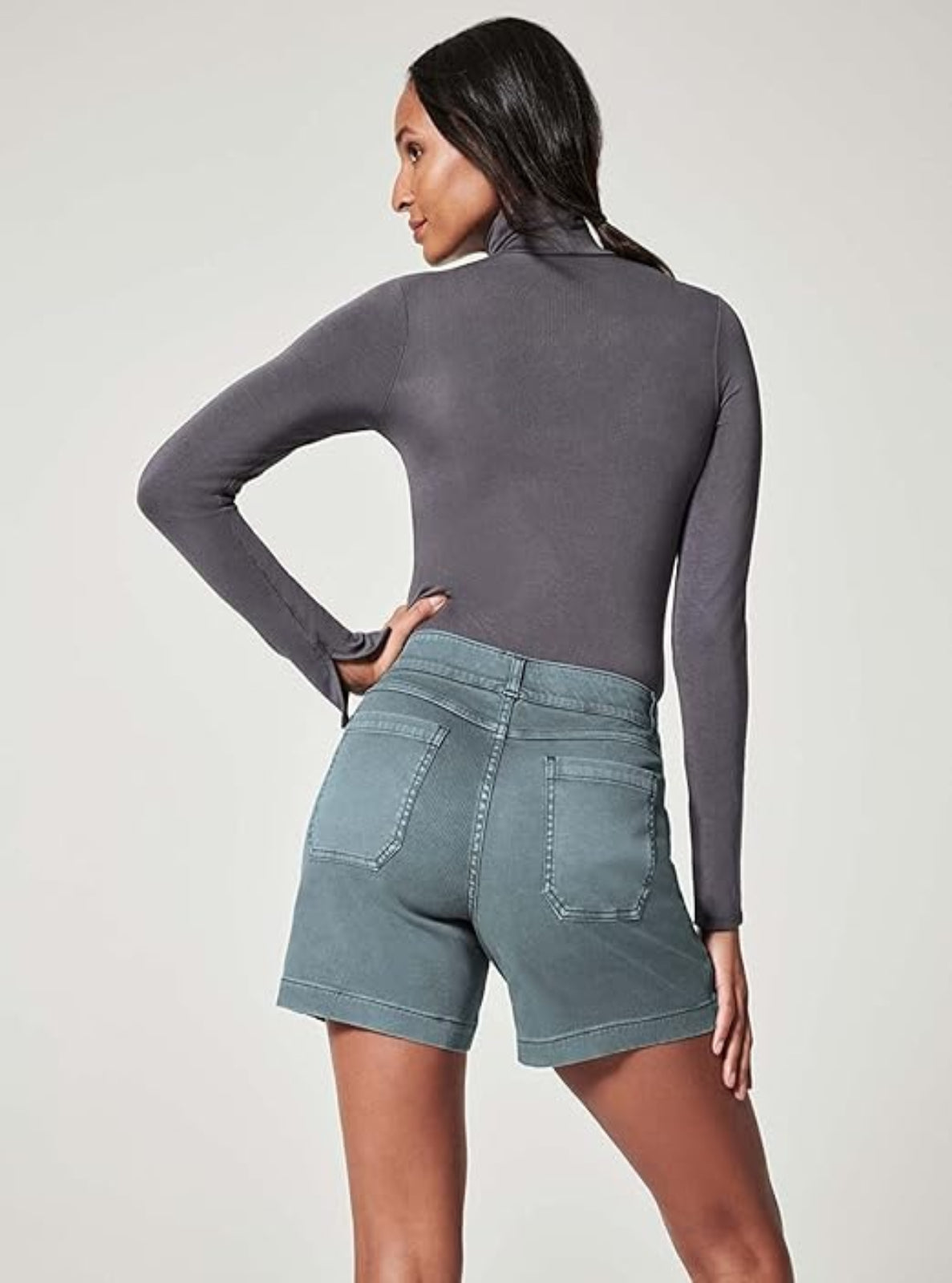 Woman wearing a gray long-sleeve top and denim shorts on a plain background
