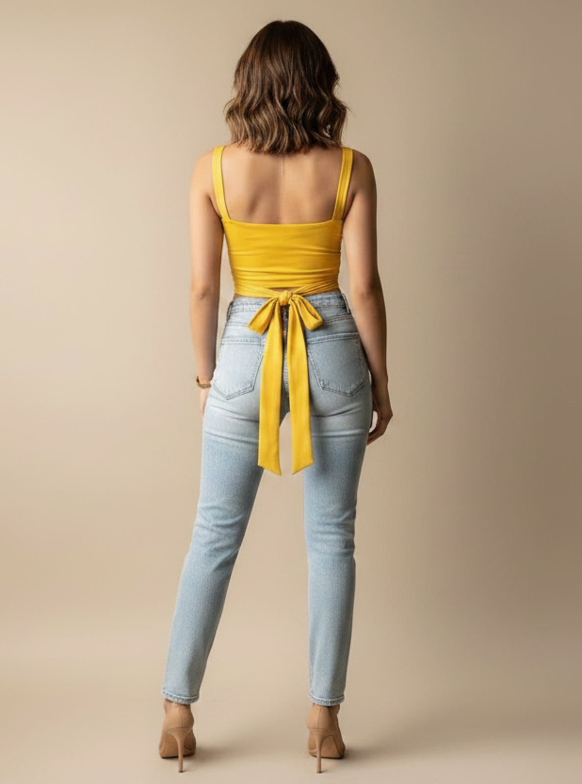 Woman wearing a yellow top and light blue jeans on a beige background
