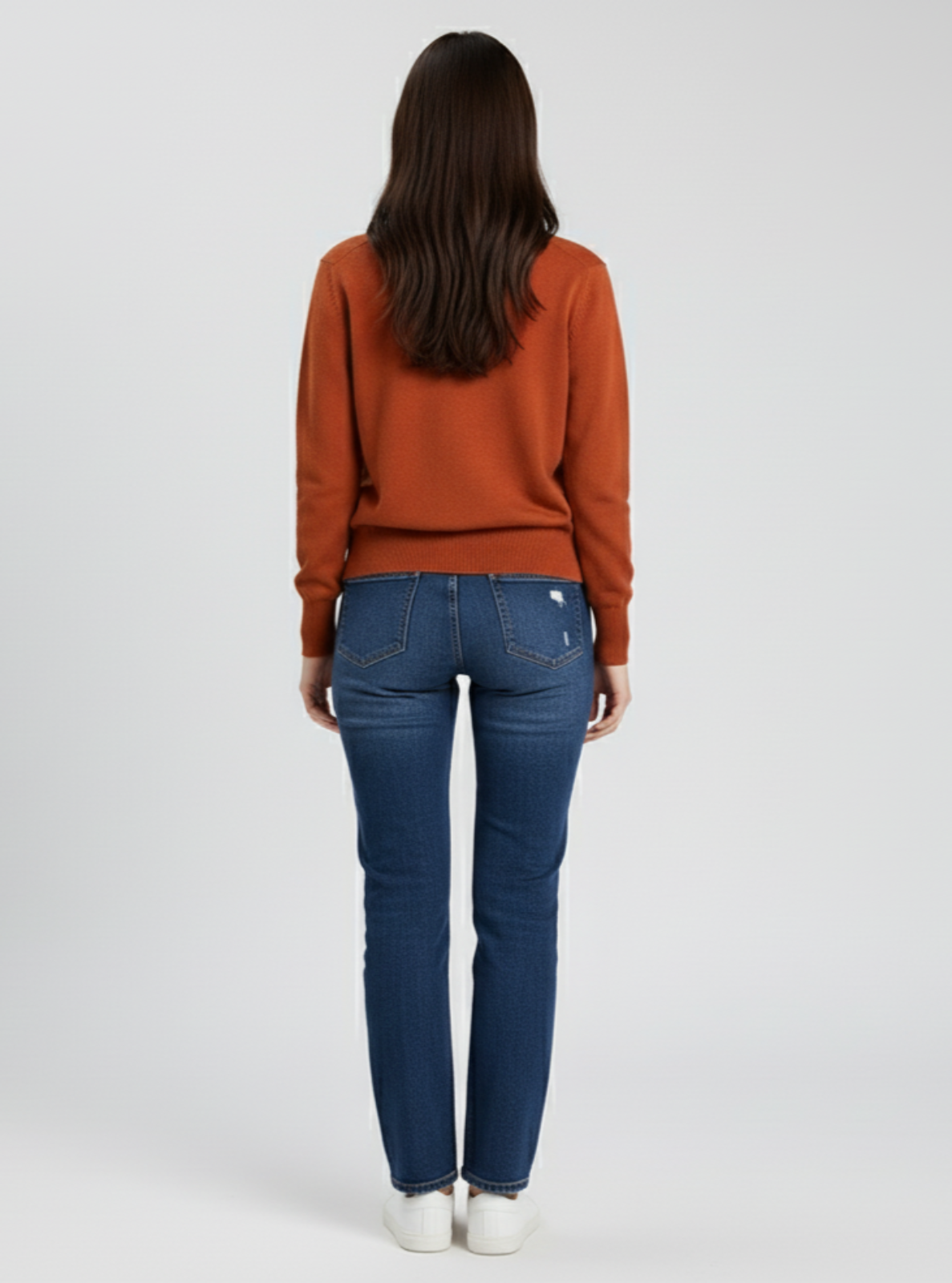 Person wearing a rust-colored sweater and blue jeans on a white background