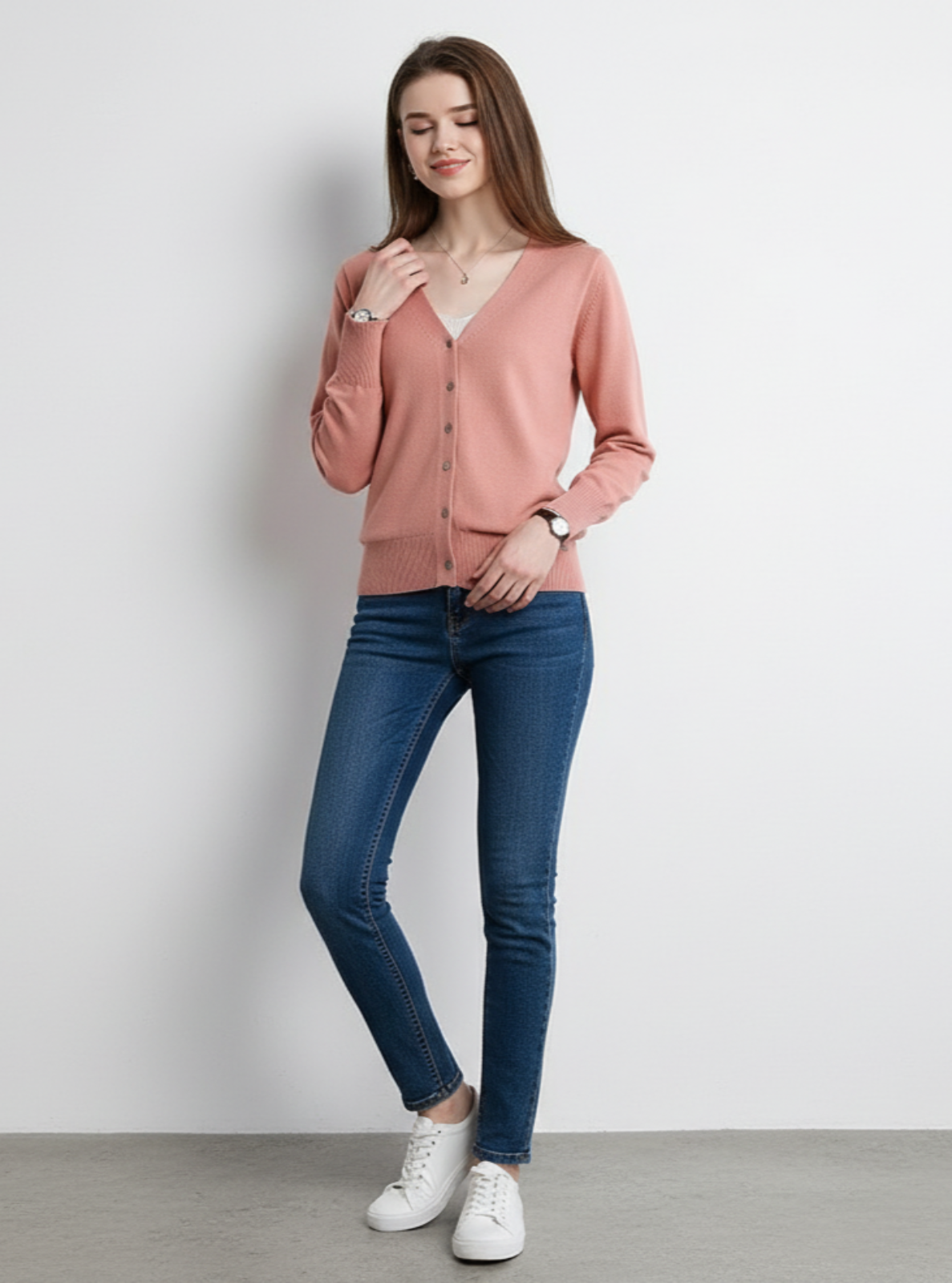 Woman wearing a pink cardigan, blue jeans, and white sneakers on a plain background