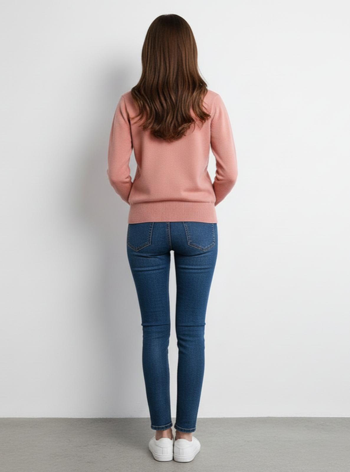 Person wearing a pink sweater and blue jeans against a white background