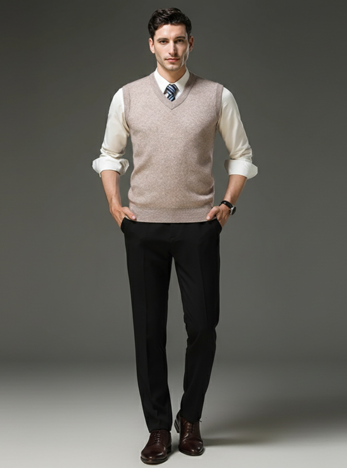 Man wearing a beige vest over a white shirt with black pants on a gray background