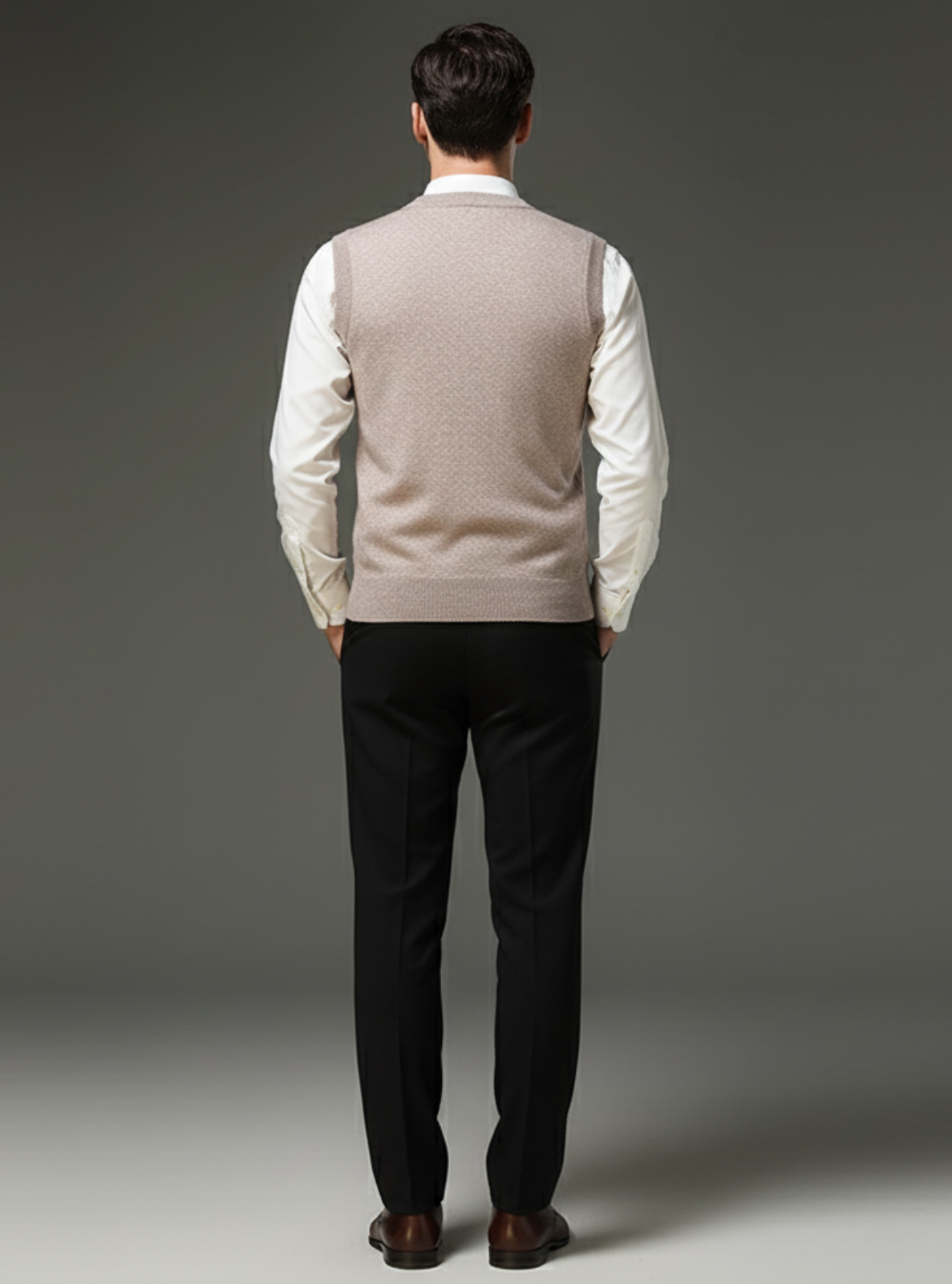 Man wearing a beige vest over a white shirt with black pants on a gray background
