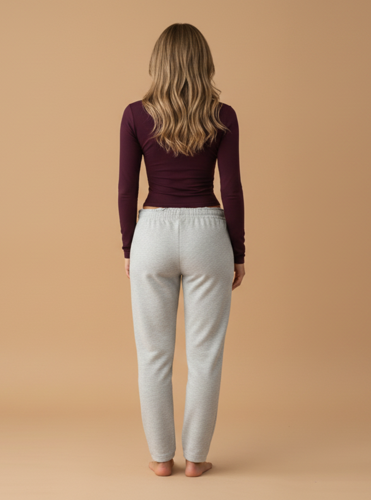 Woman wearing a purple long-sleeve top and light gray pants on a beige background