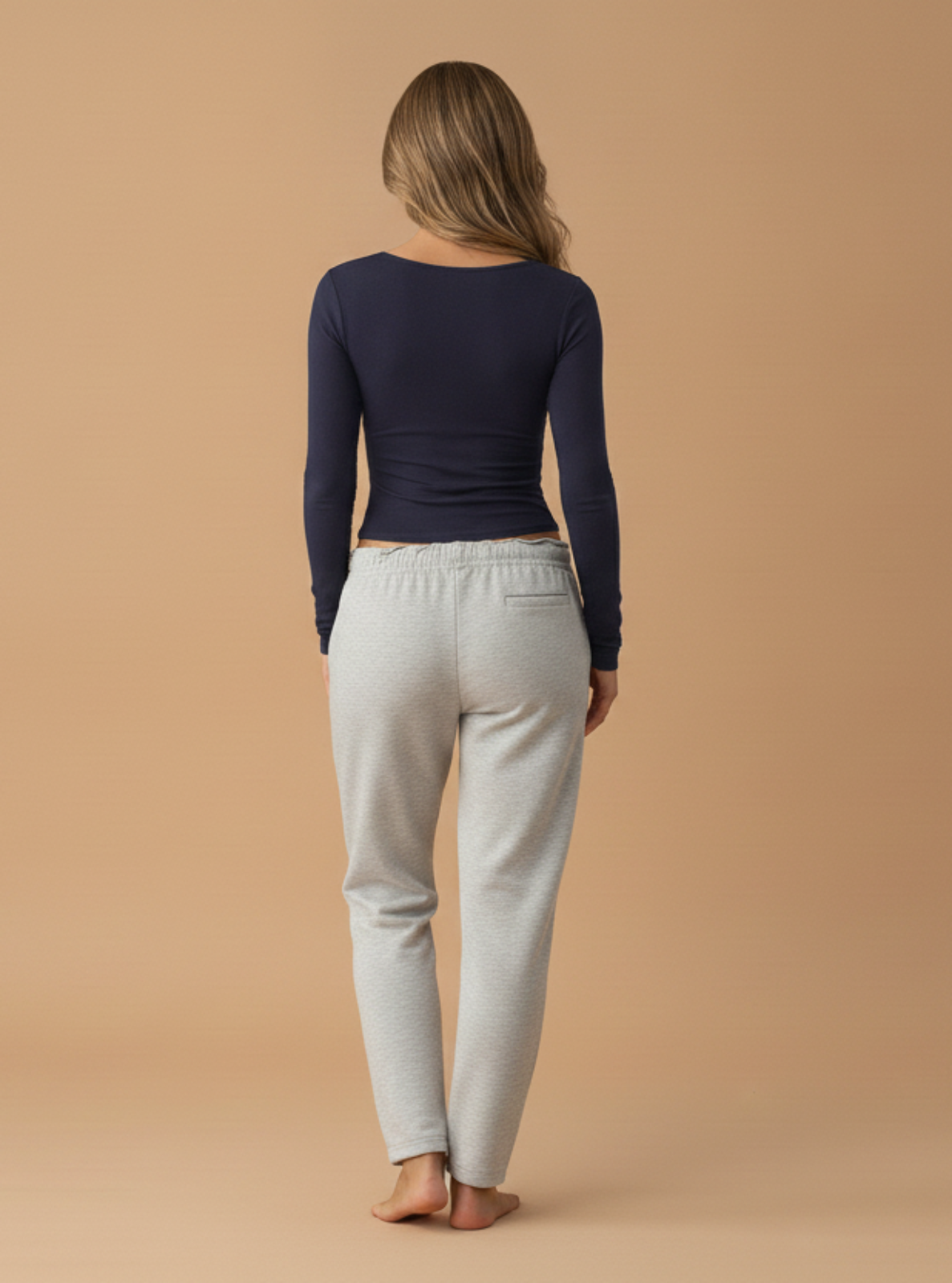 Person wearing a navy long-sleeve top and light gray pants on a beige background