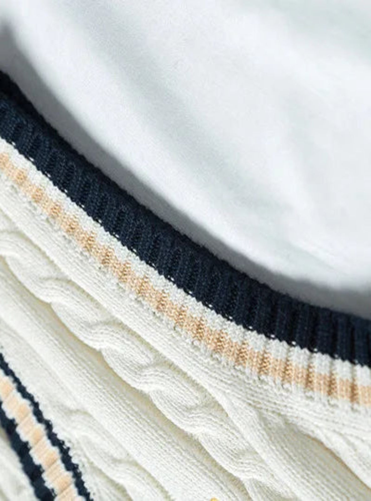 Close-up of a white sweater with navy and beige ribbed trim on a plain background