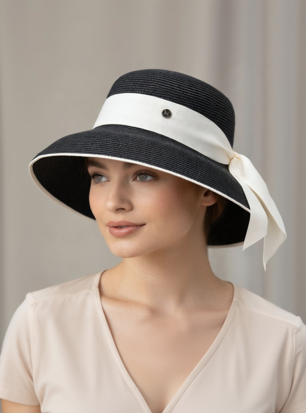 Woman wearing a black sun hat with a white ribbon on a neutral background
