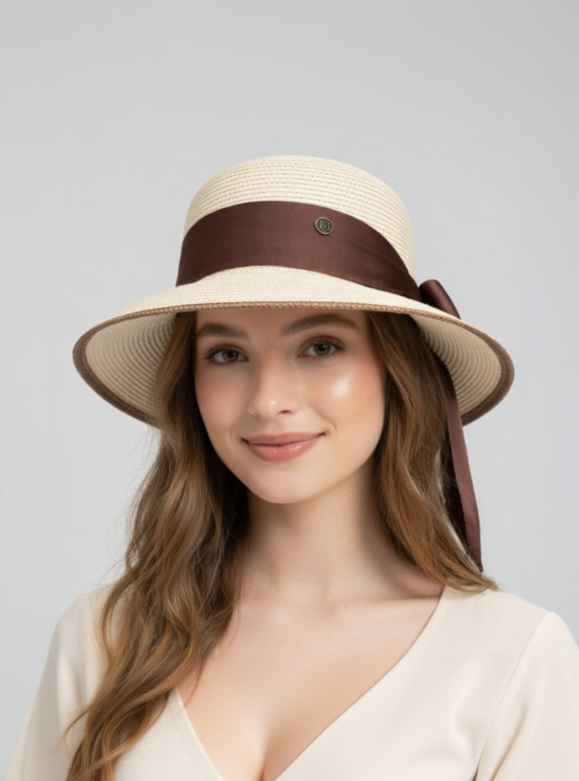 Woman wearing a beige sun hat with a brown band on a gray background