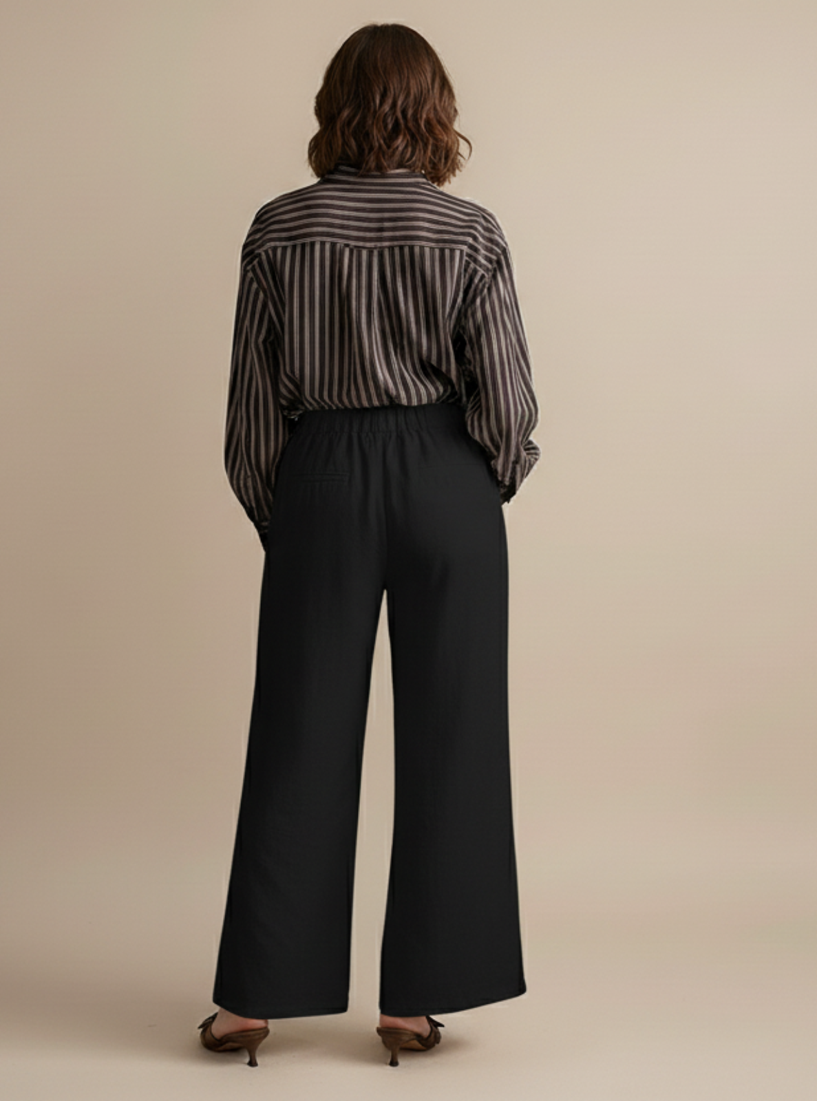 Person wearing a striped shirt and black pants on a beige background