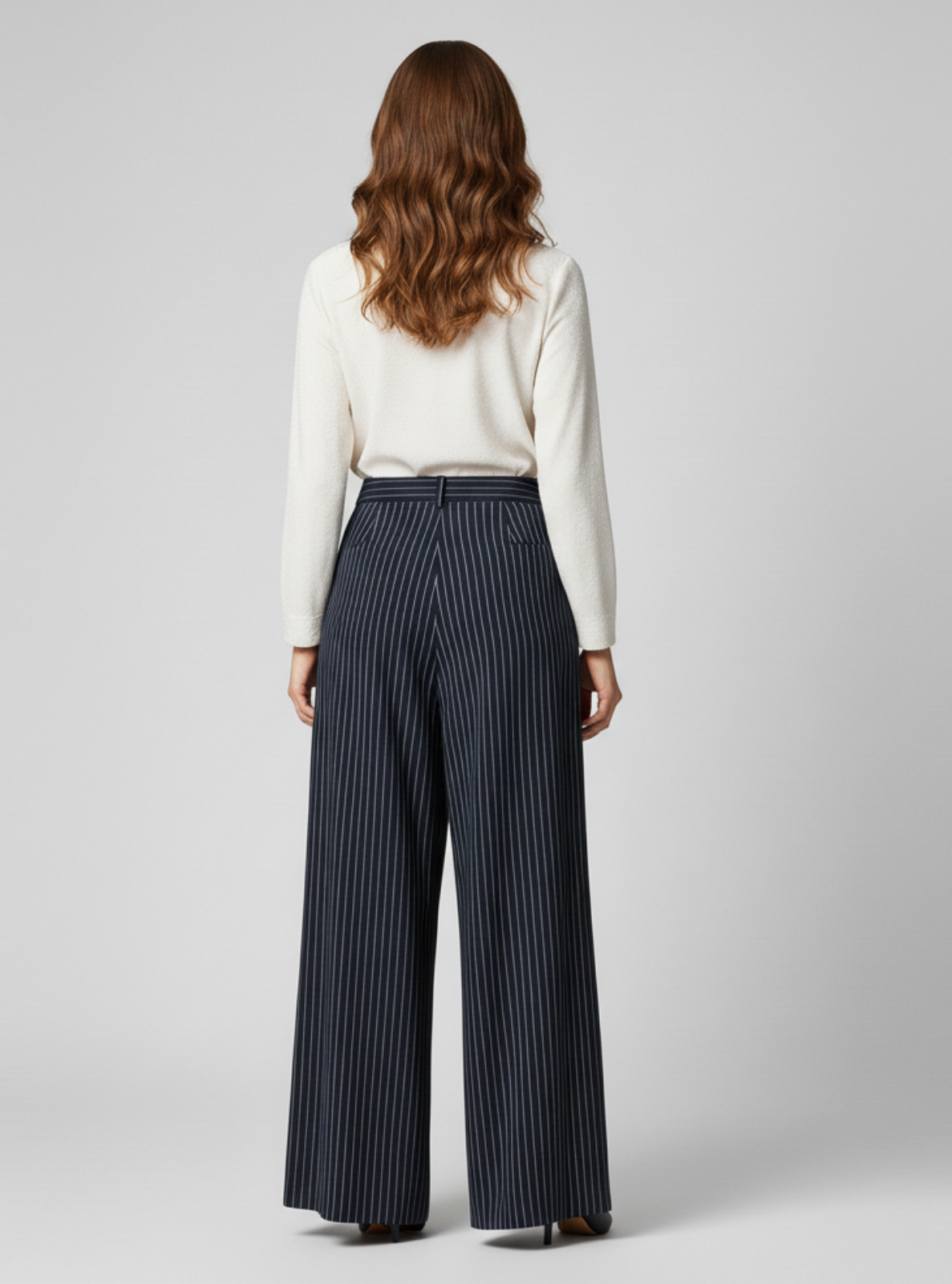 Woman wearing a white blouse and navy pinstripe pants on a gray background