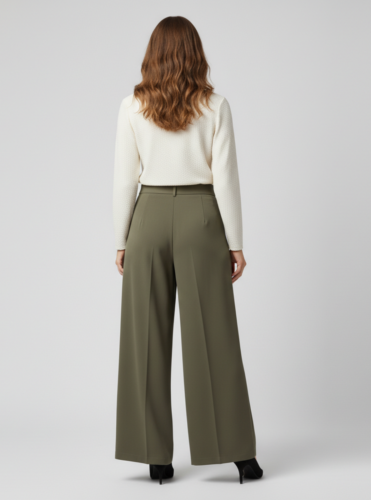 Woman wearing a white sweater and olive green wide-leg pants on a light gray background