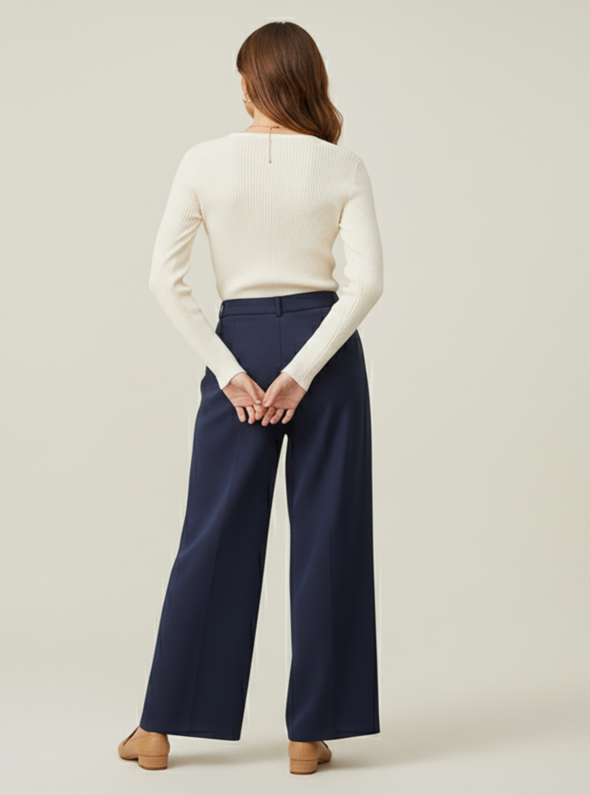 Woman wearing a white long-sleeve top and navy wide-leg pants on a beige background