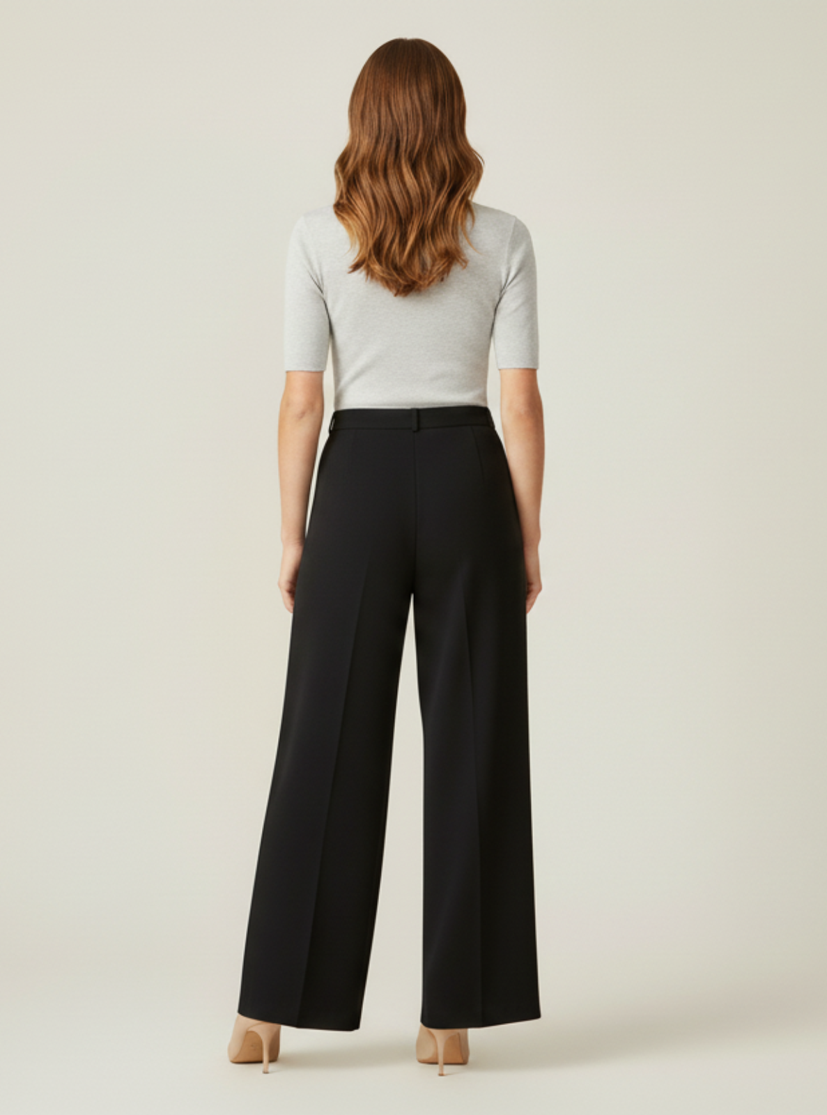 Woman wearing a white top and black high-waisted pants on a beige background