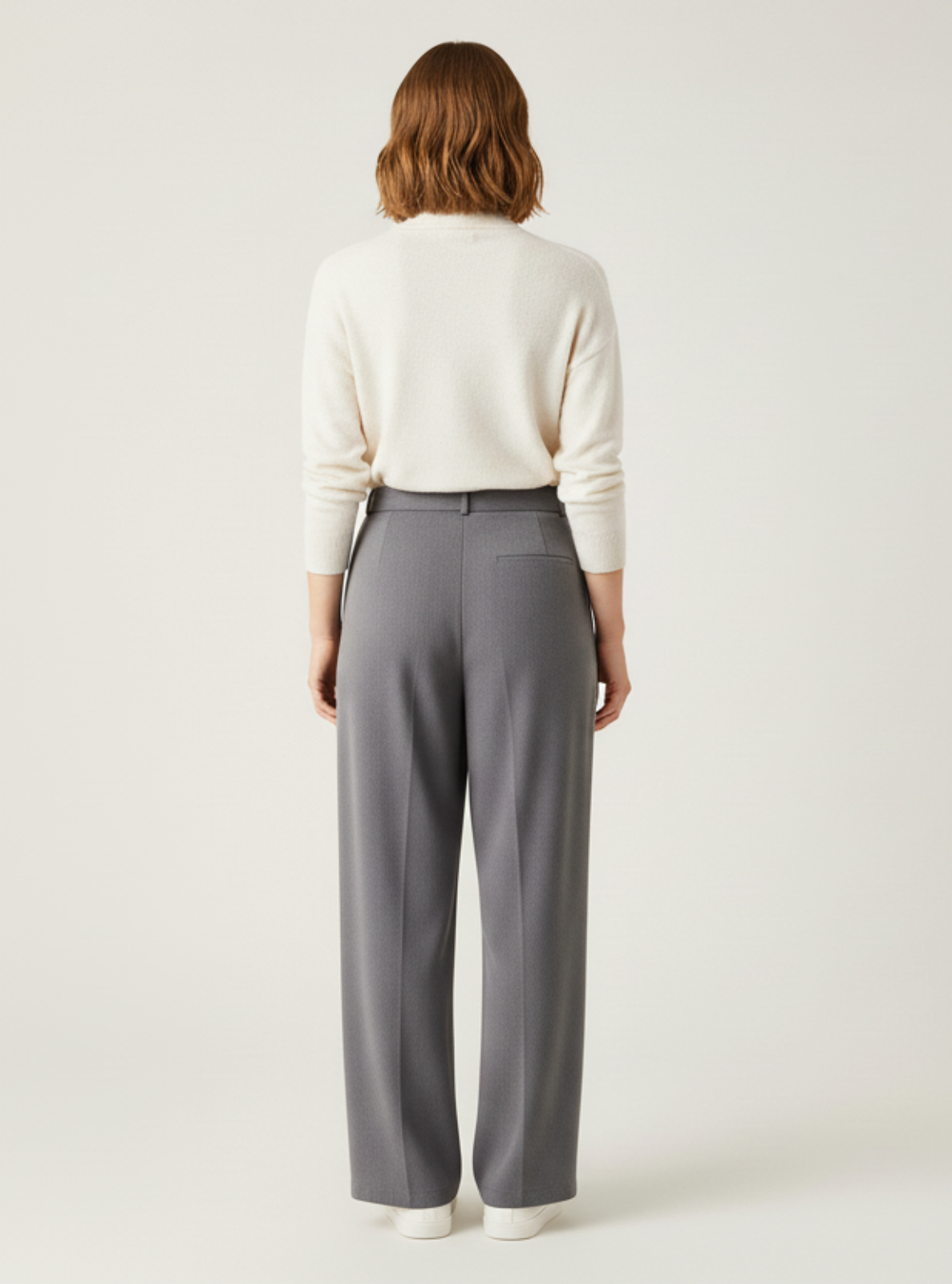 Person wearing a white sweater and gray pants on a plain background
