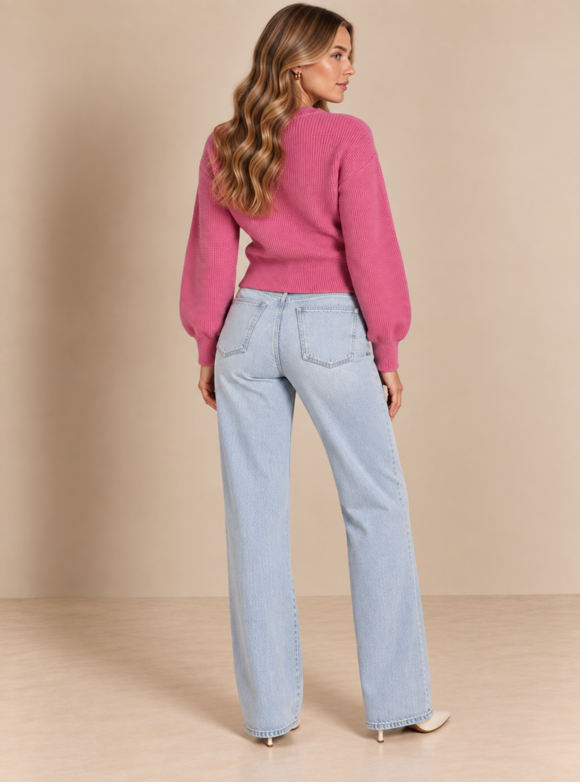A woman shown from the back wearing a pink knit sweater and light-wash wide-leg jeans, standing against a plain beige studio backdrop.