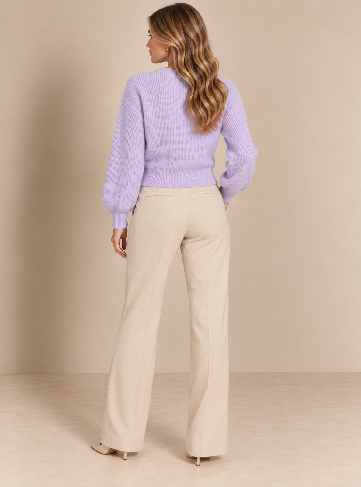 A woman shown from the back wearing a light purple knit sweater and beige wide-leg trousers, standing against a plain beige studio backdrop.