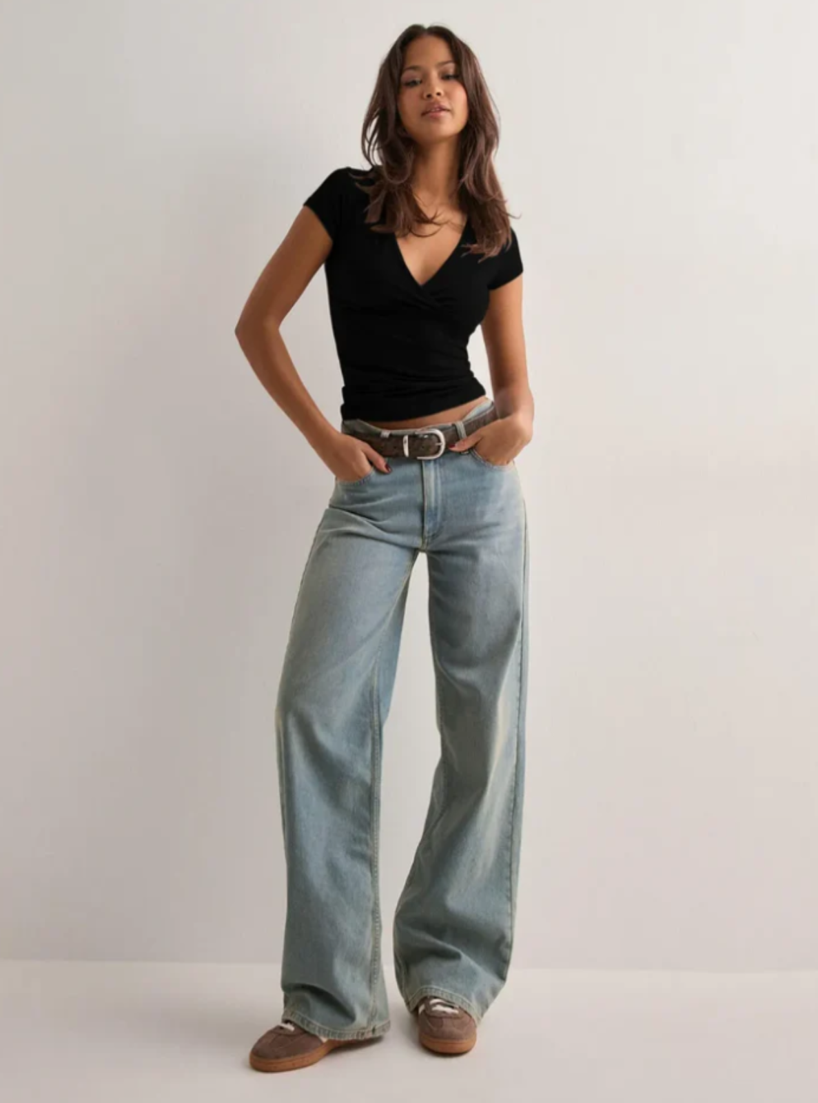 Woman wearing a black top and light blue jeans on a plain background