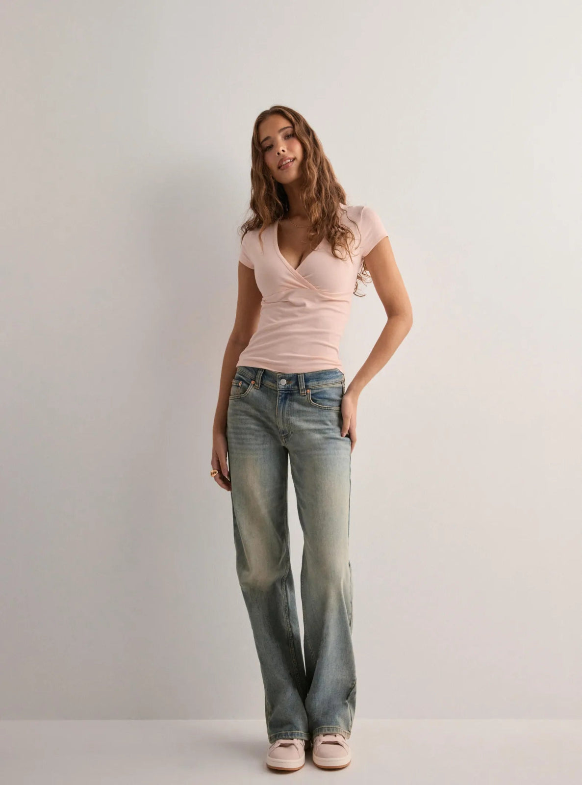 Woman wearing a pink top and blue jeans against a plain background