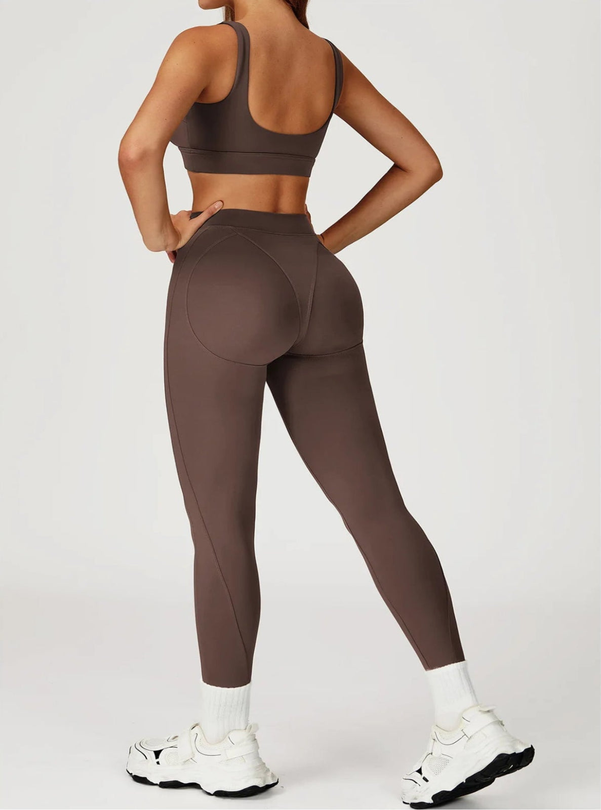 Person wearing brown athletic leggings and sports bra on a white background