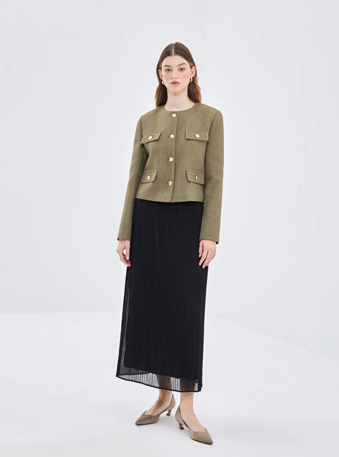 Model wearing a a khaki textured Jacket with gold buttons and a skirt with heels on a white background 