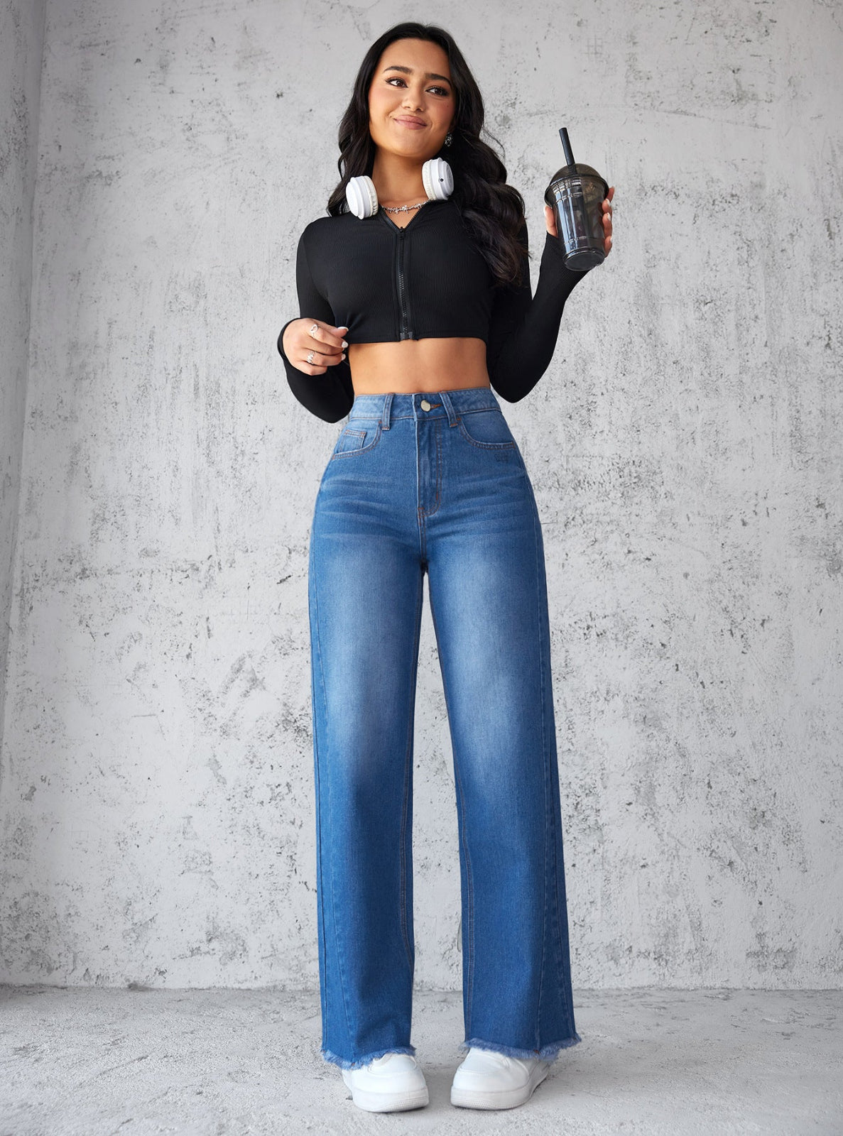 Person wearing blue jeans and a black long-sleeve top against a gray textured wall.
